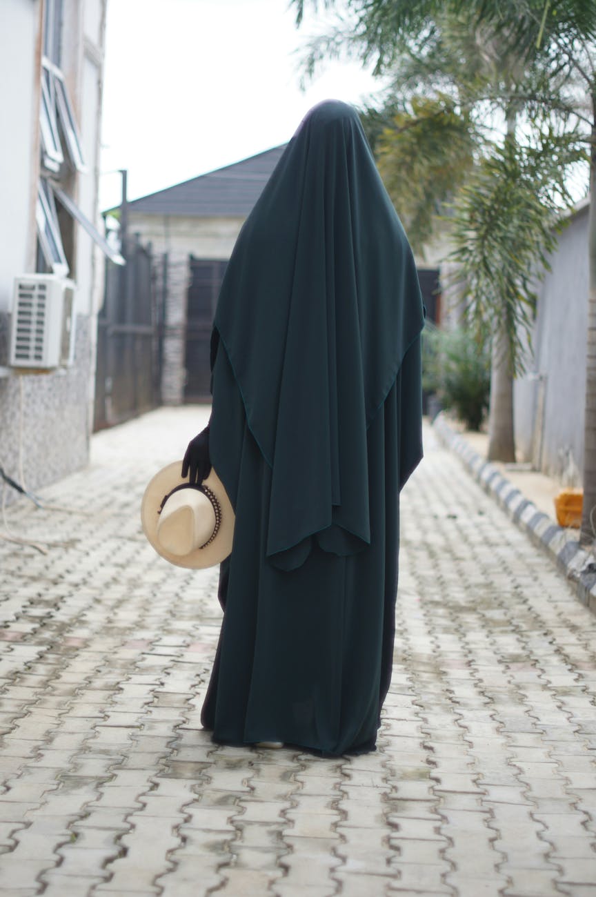 woman in jilbaab walking outdoors holding hat
